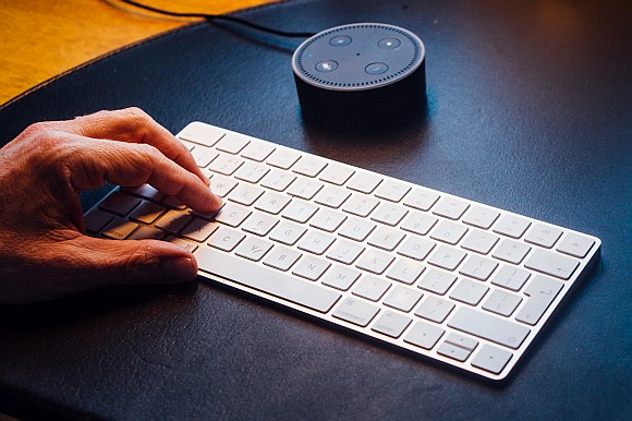 Hand typing on keyboard next to a smart speaker